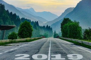 Road leading to a forest and mountains with "2019" printed on it