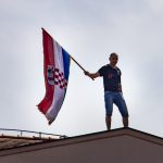 Man holding Croatian flag, standing on a rooftop